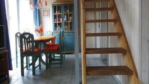 A dining area with a wooden staircase, a blue cabinet with glass doors, and a window with curtains. - Ferienhaus im skandinavischen Stil (Granzow)