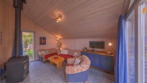 Un salon chaleureux avec une cheminée, un ensemble de canapés, une table en bois et un coin cuisine avec des meubles bleus.