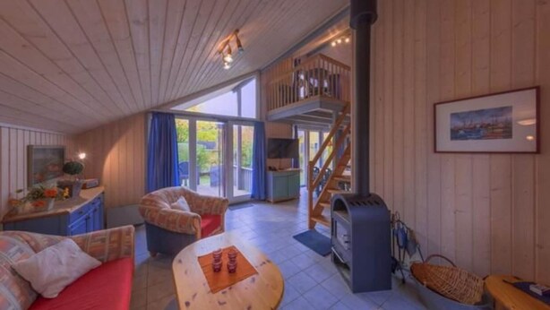 Un vaste espace de vie doté d’un plafond en bois, d’un canapé, d’une table avec des tasses, d’une cheminée et d’un escalier menant à un niveau supérieur.