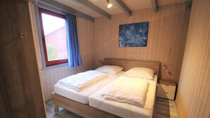 Ein Schlafzimmer mit Holzwänden, einem Doppelbett, einem Fenster mit Vorhängen und einem Gemälde an der Wand.