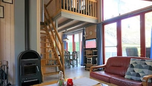 Una sala de estar acogedora con chimenea, un sofá rojo, una escalera de madera y un televisor.