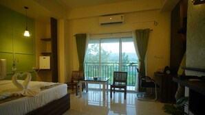 A hotel room with a bed, a table, chairs, a balcony with curtains, and a potted plant. - Hotel Garnet (Bokakhat)