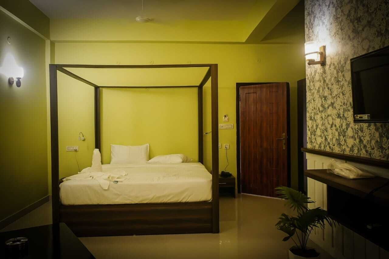 A four-poster bed in a room with green walls, a wooden door, and a television on the wall.