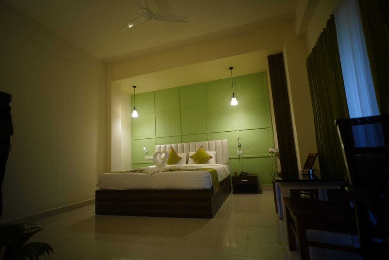 Una habitación de hotel con una cama grande, una pared de acento verde e iluminación colgante.