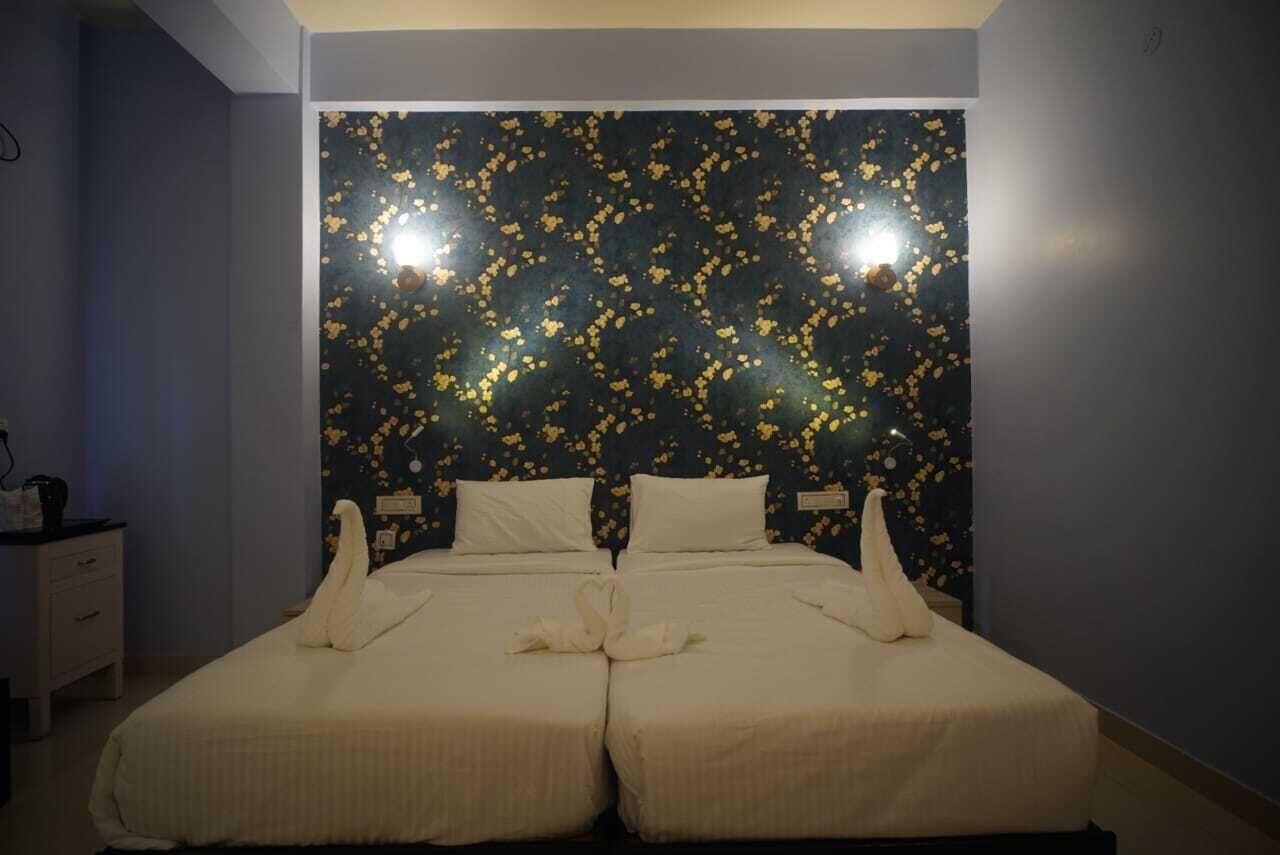 A double bed with white linens and two pillows, a nightstand with a lamp, and a wall with a dark floral pattern.