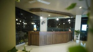A reception area with a wooden counter, glass walls, and pendant lighting. - Hotel Garnet (Bokakhat)