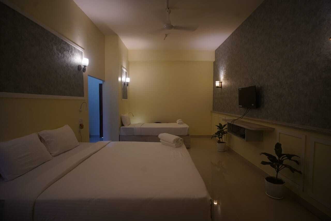 A hotel room with a large bed, a smaller bed, a TV, and a plant.