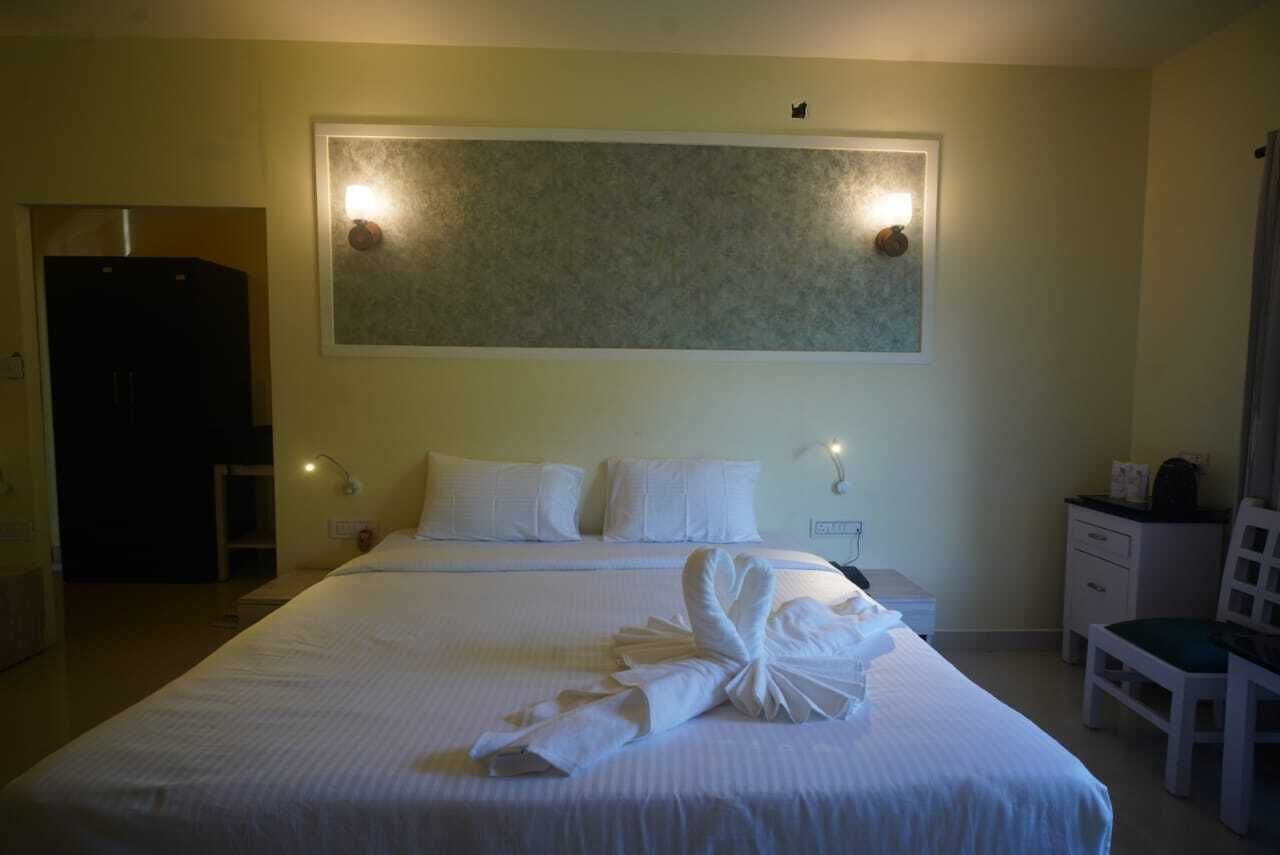A hotel room with a large bed, two bedside lamps, a headboard with lights, a desk, and a chair.