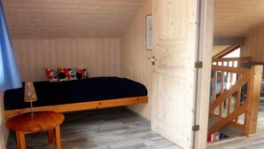 Una habitación pequeña con paneles de madera, una cama, una mesita y una puerta que da a otra habitación.