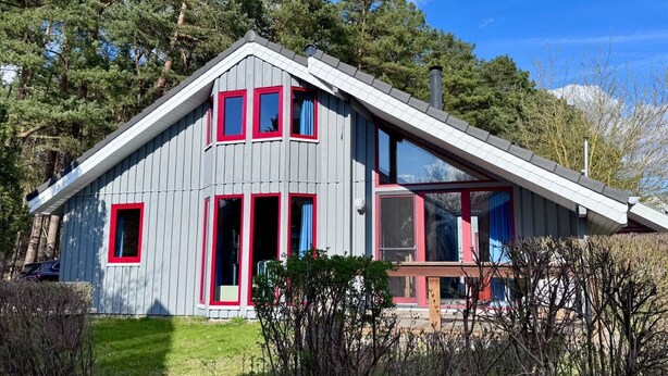 Una casa moderna con techo inclinado, ventanas grandes y detalles en rojo.