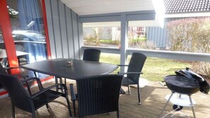 Un patio cubierto con mesa y sillas, una parrilla de barbacoa y vistas a una zona residencial.