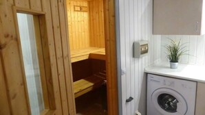 Una sauna de madera con bancos, una lavadora y una pequeña planta en maceta sobre un mostrador.