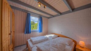 A bedroom with a wooden bed, a window with blue curtains, and a white brick wall.