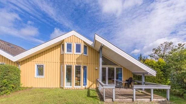 A yellow wooden house with a sloped roof, large windows, and a covered porch.