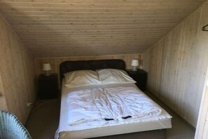 Ein schmales Zimmer mit Holzvertäfelung, einem Einzelbett, zwei Nachttischen und einem Sessel.