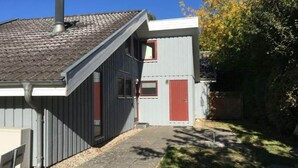 Un piccolo edificio a un piano con tetto spiovente e una porta rossa.