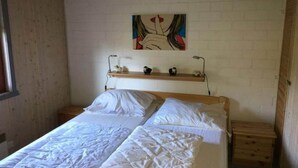 Una camera da letto con due letti, una testiera in legno, una parete di mattoni bianchi e uno scaffale con oggetti decorativi.
