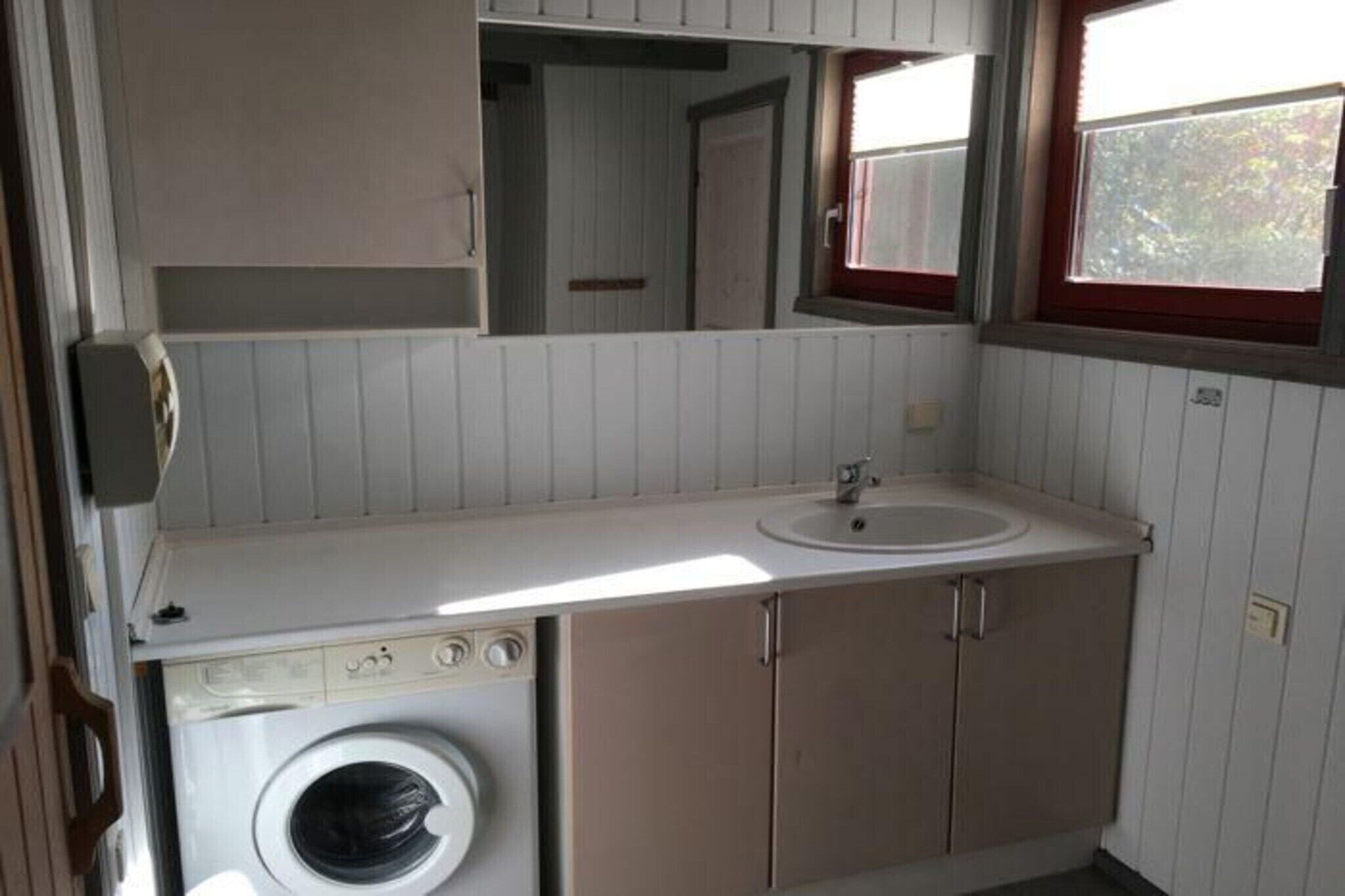 A compact bathroom with a washing machine, a sink, and a mirror.