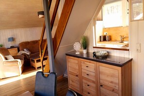Un dormitorio estilo loft acogedor con techo inclinado, una mesa de comedor de madera, un sofá y una kitchenette con fregadero y tostadora.