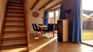 Et værelse med en trætrappe, et spiseområde med et bord og stole, et køleskab og et stort vindue med gardiner.