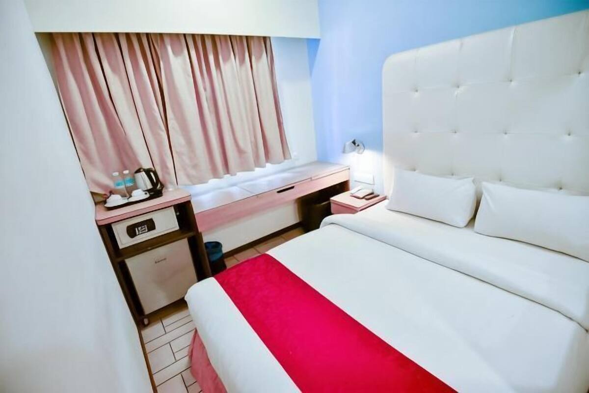A hotel room with a bed, a desk, a lamp, and a window with curtains.