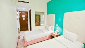 Une chambre d’hôtel avec deux lits, une fenêtre, une porte et une petite table de chevet avec une lampe.
