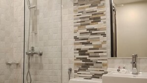 Une douche avec une porte en verre, des toilettes et un lavabo avec un miroir.