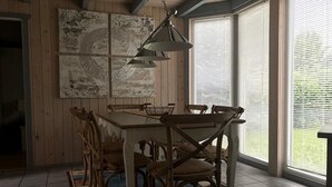 Un comedor con mesa y sillas de madera, una lámpara colgante y una ventana con persianas.