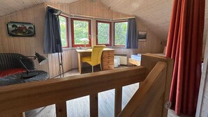 A cozy attic bedroom with a wooden ceiling, a desk with a chair, and a window overlooking greenery. - exklusives skandinavisches Ferienhaus (Granzow)