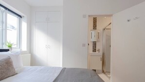 A bedroom with a bed, a window, a wardrobe, and a bathroom visible through an open door. - Ealing 3 Bath Flat w/ Parking | 10 mins to Station (London)
