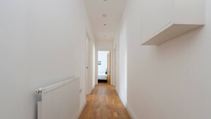 A narrow hallway with wooden flooring, white walls, and a radiator on the left. - Ealing 3 Bath Flat w/ Parking | 10 mins to Station (London)