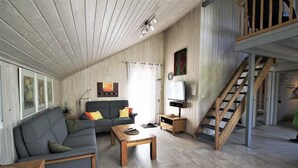 A spacious living room with a high ceiling, a sofa, a coffee table, a TV, and a staircase. - Ferienhaus im Ferienpark Mirow (Granzow)