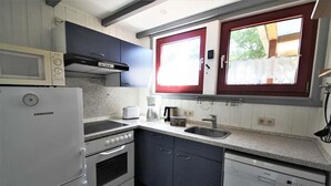 A compact kitchen with a Liebherr refrigerator, a microwave, a stove, a sink, and a dishwasher. - Ferienhaus im Ferienpark Mirow (Granzow)