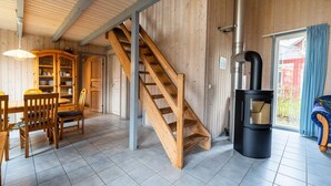 Interior de fusta amb una escala, una zona de menjador i un bressol de llenya.