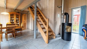 A wooden interior with a staircase, a dining area, and a wood stove.