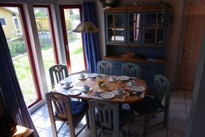 Een eetgedeelte met een ronde tafel gedekt voor vier personen, omringd door stoelen. Aan de rechterkant van de tafel bevindt zich een kast met glazen deuren.