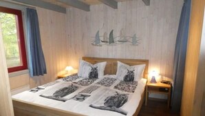 Un lit en bois avec un couvre-lit à motifs, deux lampes de chevet et une fresque murale représentant des voiliers.