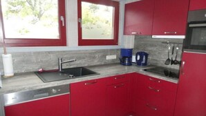 Une cuisine avec des meubles de couleur rouge, un évier en acier inoxydable, une machine à café et une fenêtre donnant sur un paysage verdoyant.