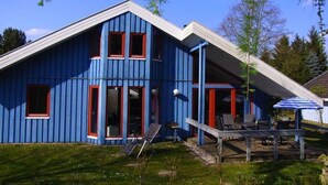 Une maison bleue avec un toit en pente, une terrasse couverte avec des chaises et une petite plateforme.
