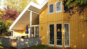 Una casa amarilla con porche cubierto, ventanas amplias y una pequeña terraza.