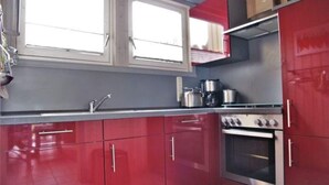 Una cocina con armarios rojos, un horno de acero inoxidable y una ventana sobre el fregadero.