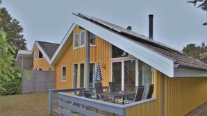 Una casa amarilla con techo gris, una chimenea y un patio con mesa y sillas.
