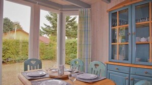 Un comedor con una mesa de madera dispuesta para cuatro personas, un aparador azul con puertas de cristal y vistas a un jardín.