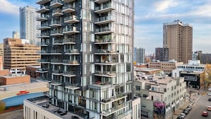 Un edificio de gran altura con varios balcones, un estacionamiento y edificios urbanos circundantes.