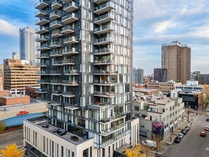 Um edifício alto com várias varandas, estacionamento e prédios urbanos ao redor.