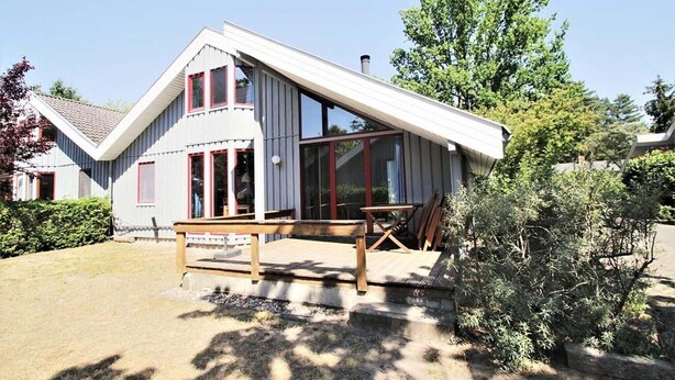 Una casa moderna con techo inclinado, ventanas amplias y una terraza de madera.