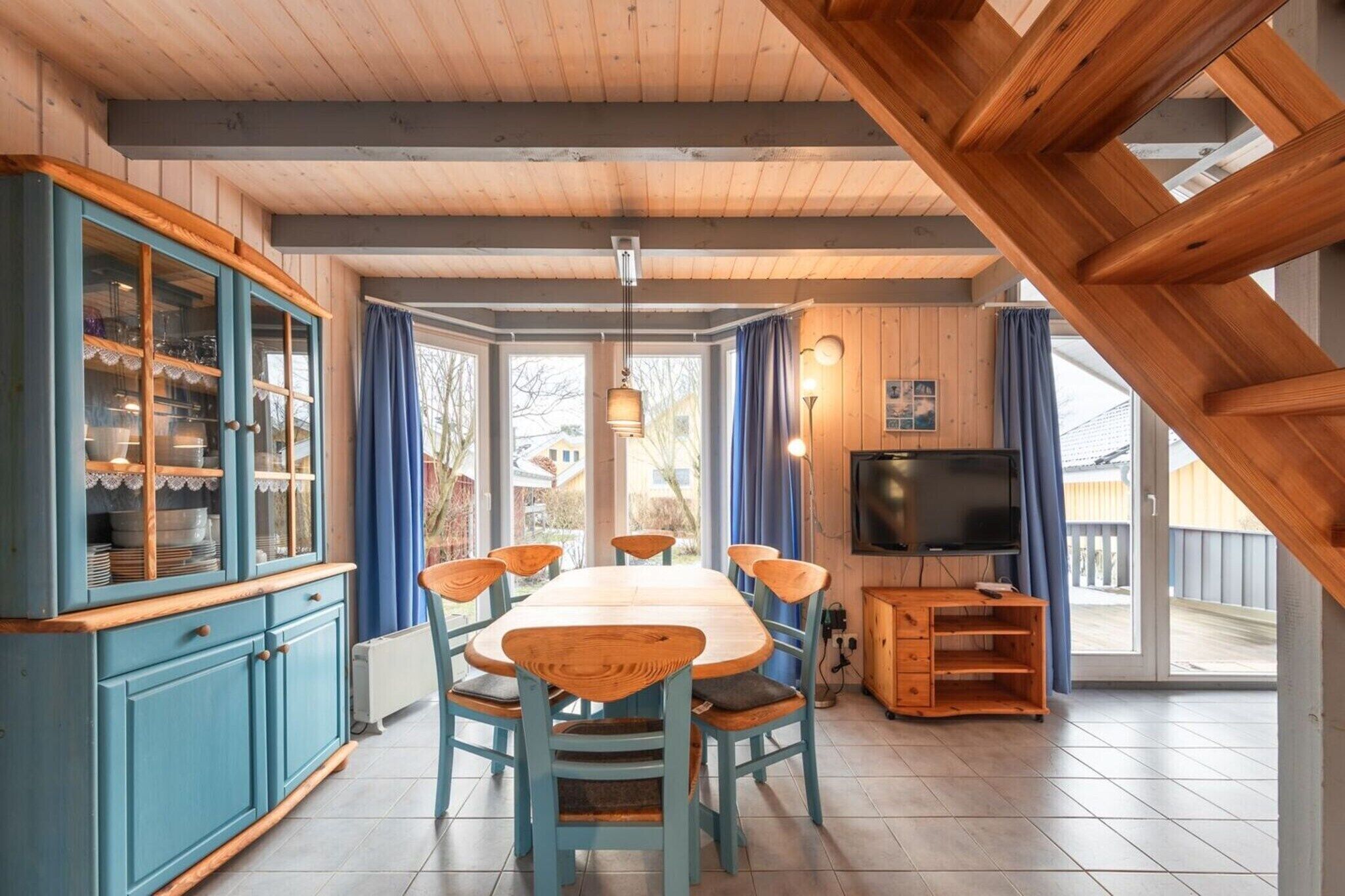 Ein Essbereich mit einem Holztisch und Stühlen, einer blauen Kommode mit Glastüren, einem Fernseher und Blick durch große Fenster.