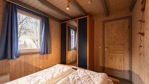 Una habitación con paneles de madera, una cama, una ventana con cortinas y una puerta.