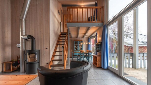 Un interior moderno con una escalera de madera, una chimenea y ventanas amplias.