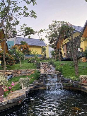 A garden with a small waterfall, stone steps, and a variety of plants. - Linh Anh Homestay Moc Chau - BAY LUXURY (Thao Nguyen)